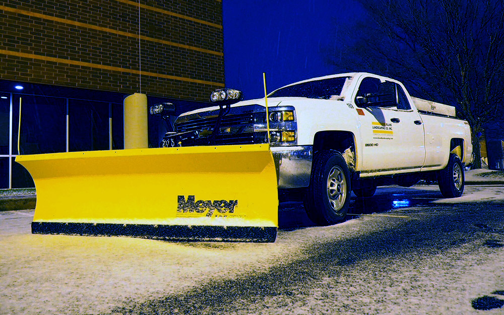 A Bland truck with an attached snow plow at night