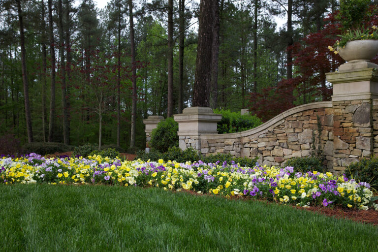 Turfgrass, purple and yellow flowers, and a stone structure at Governors Club